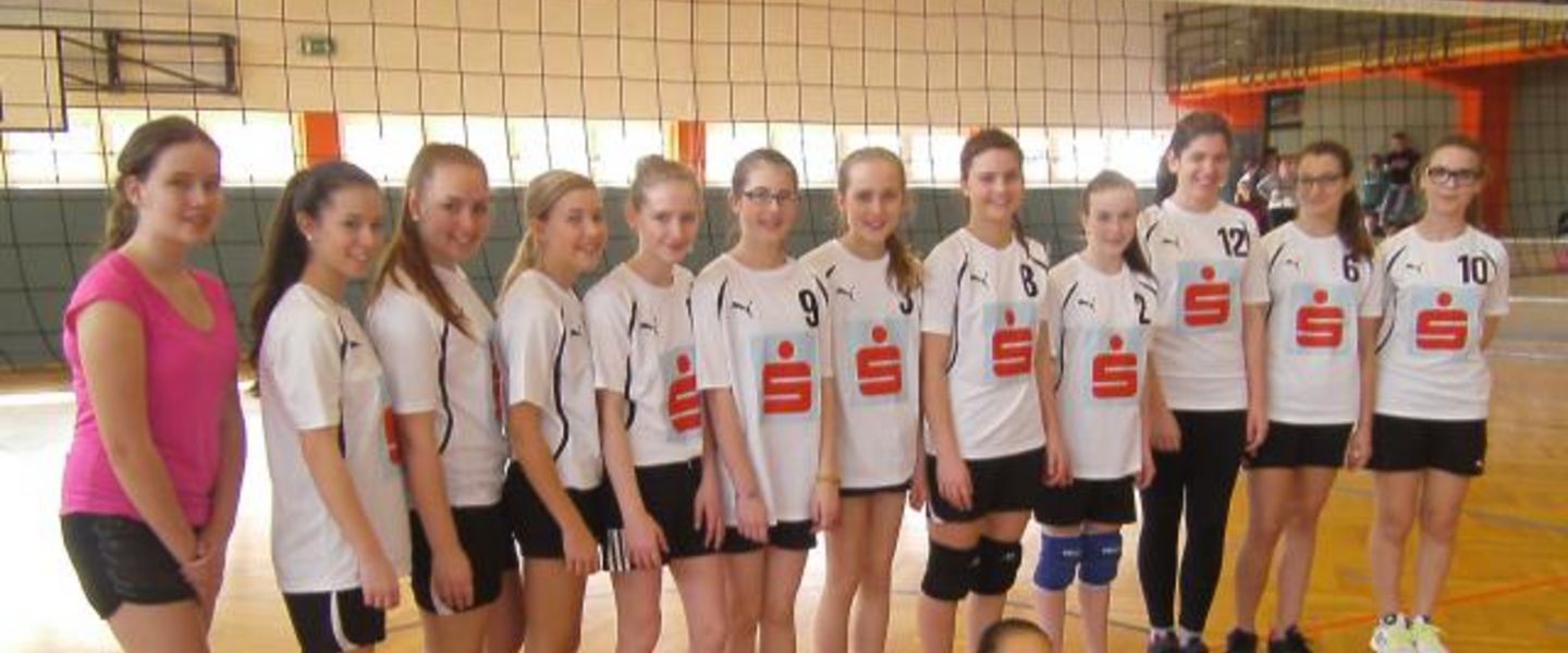Mädchenmannschaft posiert vor Volleyballnetz